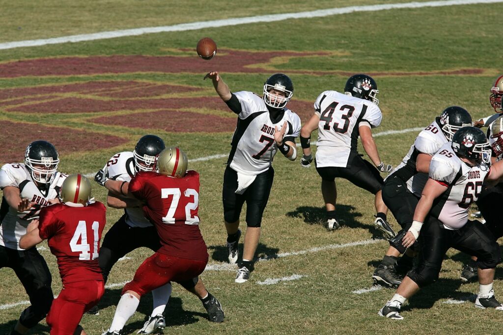 College quarterback passes the football while his teammates protect him from onrushing opponents.